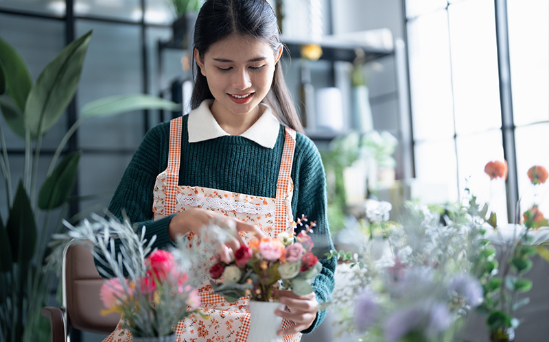 smiling-florist-arranging-colorful-flowers-in-small-white-ceramic-vase